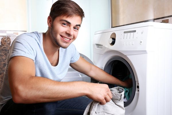 کار خانه مردی که لباس‌ها را در ماشین لباسشویی بار می‌کند