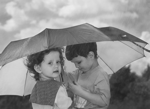 دختر و پسر کوچکی که زیر یک چتر از باران پنهان شده اند سیاه