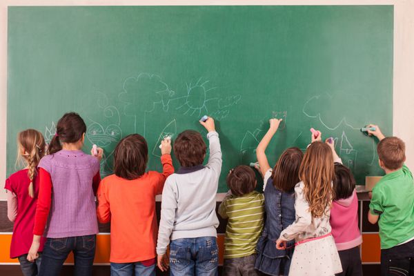 گروه نه نفری از کودکان که روی تخته سیاه مدرسه با گچ نقاشی می کنند