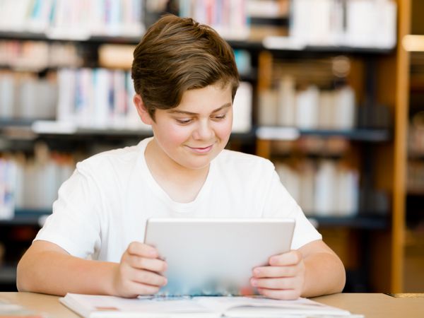 پسر نوجوان با تبلت در کتابخانه