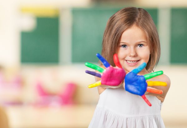 بچه بچه ای شاد که با رنگ در انگشتانش بازی می کند