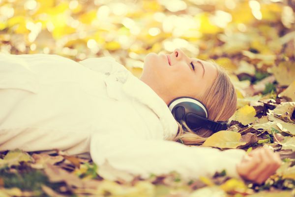 زن جوان شاد در حال گوش دادن به موسیقی در پارک عمداً با صدای بلند