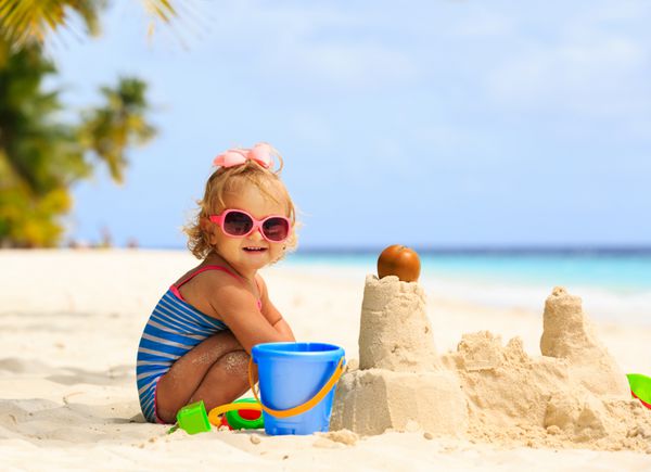 دختر بچه ناز در حال بازی با شن و ماسه در ساحل