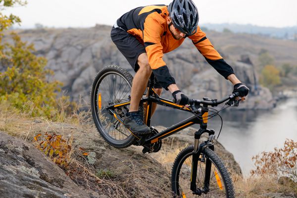 دوچرخه سواری با لباس نارنجی در حال دوچرخه سواری در پایین تپه راکی زیر رودخانه