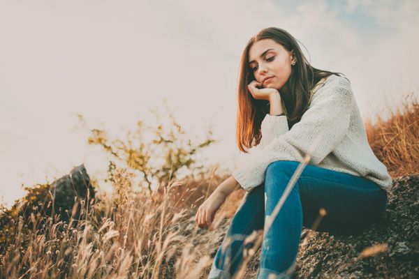 دختر نوجوانی که در روز سرد پاییزی تنها نشسته است زن جوان غمگین تنها که ژاکت گرم پوشیده و در حال فکر و تردید است مفهوم تنهایی و تنهایی