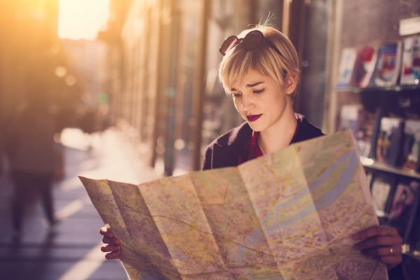 زن مسافر جوان زیبا که در خیابان ایستاده و به نقشه نگاه می کند