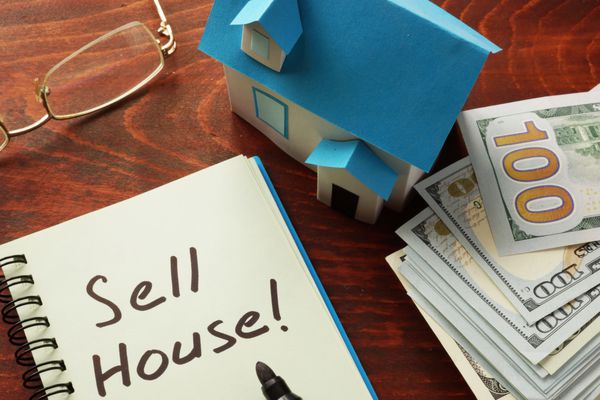 دفترچه ای با عبارت Sell house روی میز