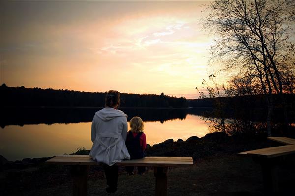 مادر و دختر کوچکش کنار هم روی نیمکت نشسته اند و غروب زیبای خورشید را زیر دریاچه تماشا می کنند