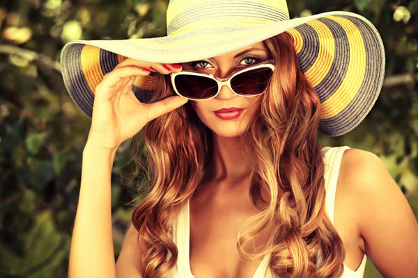 زن جوان زیبا با کلاه و عینک آفتابی زیبا که در فضای باز ژست گرفته است