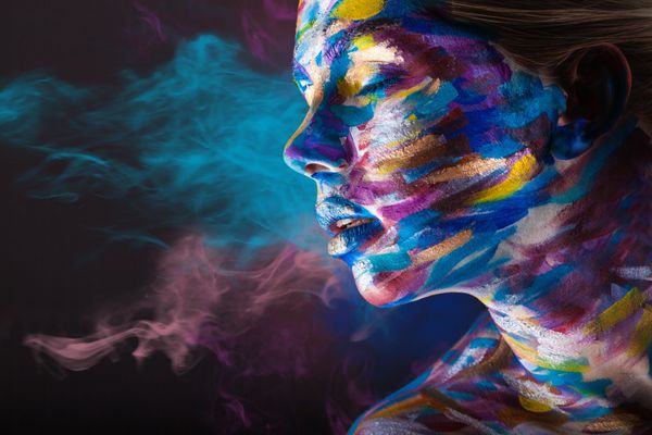 زن جوان با آرایش رنگارنگ و آرت بدن روی زمینه مشکی با دود چند رنگ