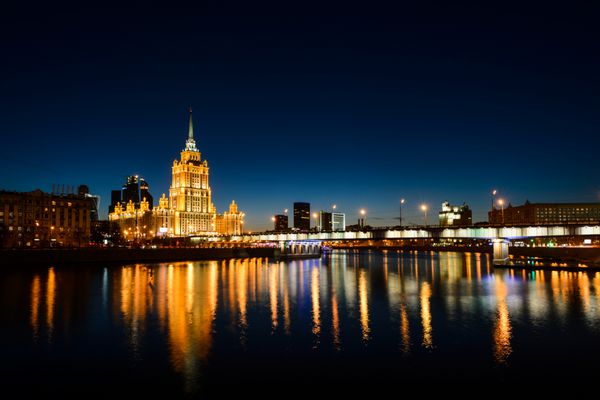 نمایی شگفت انگیز از برج استالین و چراغ های پل که در آب و رودخانه ساحل مسکو با آسمان خراش های تجاری در پایتخت روسیه روشن شده اند منظره شهر مسکو و آسمان آبی پس از غروب خورشید مسکو روسیه
