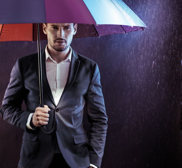 تاجر خوش تیپ زیر یک چتر ایستاده در باران واقعی