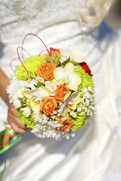 دسته گل عروسی در دستان عروس - زنی با لباس سفید که گل های رنگارنگ عروسی تازه را در دست دارد تزیین عروس شیک و کلاسیک با ارکیده های کرم رنگ شگفت انگیز و رز نارنجی برای ازدواج