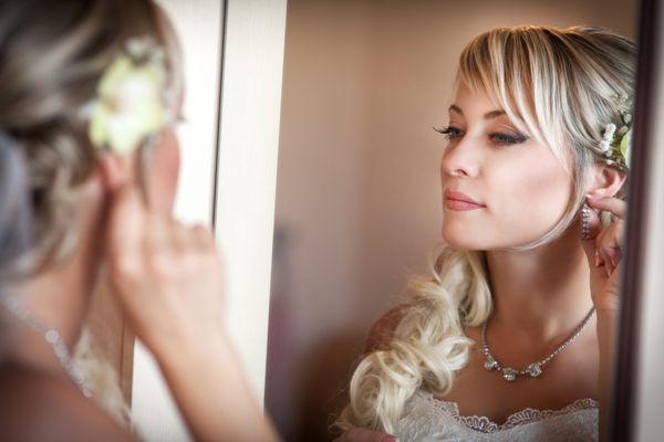 عروس زیبا با لباس عروس سفید با مدل مو و آرایش روشن دختر شاد منتظر داماد خانم رمانتیک با لباس عروس و گل در موها آماده شدن نهایی برای عروسی است