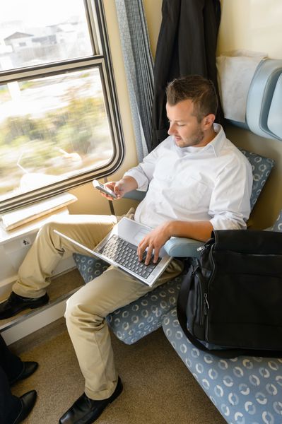 مردی که در تلفن همراه با لپ‌تاپ پیام می‌دهد قطار مسافرتی سفر کاری