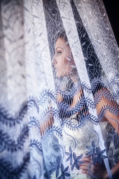 عروس زیبا با لباس عروس سفید در اتاق خوابش نزدیک پنجره ایستاده است
