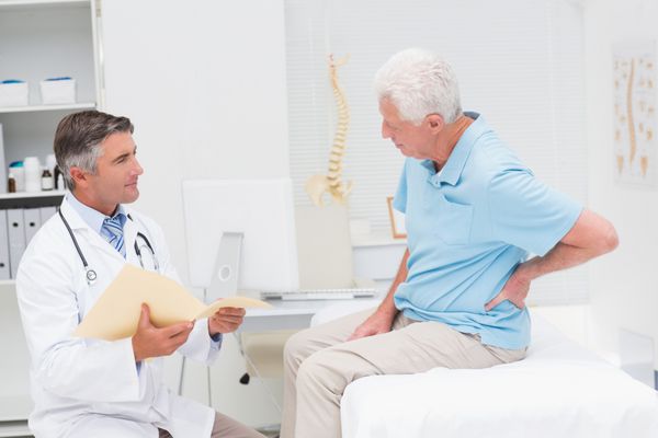 پزشک مرد در حال بحث در مورد گزارشات با بیمار ارشد مبتلا به کمردرد در کلینیک