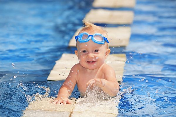 نوزاد خندان شاد با اولین دندان و عینک زیر آب با پاشیدن آب آبی شفاف در استخر قبل از آموزش شنا سبک زندگی سالم فعالیت تابستانی و آموزش شنا به کودکان