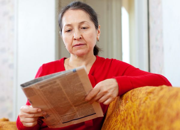 زن بالغ جدی به روزنامه در خانه نگاه می کند