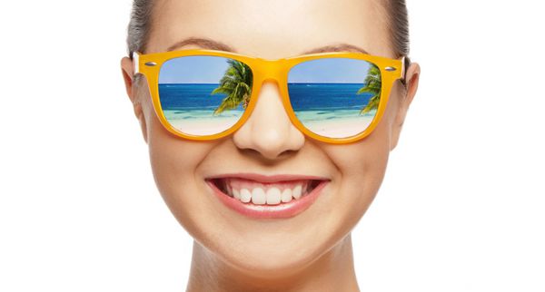 سفر تعطیلات تعطیلات تابستانی و مفهوم افراد شاد - پرتره دختر نوجوان شاد با عینک آفتابی با انعکاس ساحل