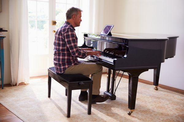 مردی در حال یادگیری نواختن پیانو با استفاده از برنامه تبلت دیجیتال