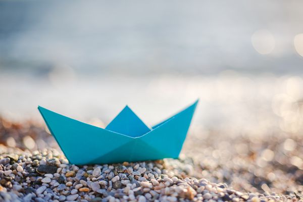 قایق کاغذی آبی در ساحل سنگریزه ای