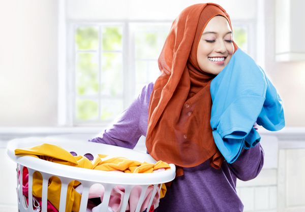 پرتره زن جوان با حجاب در حالی که سبد لباس را حمل می کند در حالی که بوی لباس های تمیز تازه را می دهد