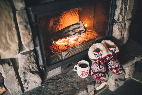 دمپایی راحت کریسمس در کنار شومینه دنج گرم فضایی آرامش‌بخش در کلبه‌ای با آتش‌سوزی قدیمی قدیمی با یک فنجان نوشیدنی مفهوم تعطیلات زمستانی و کریسمس