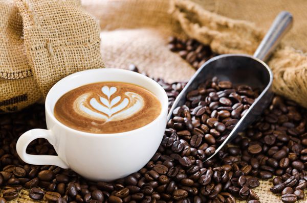 فنجان قهوه سفید و دانه های قهوه برشته شده در اطراف