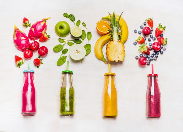 مجموعه ای از اسموتی های میوه و سبزیجات در بطری های شیشه ای با نی روی زمینه چوبی سفید ترکیبات تازه ارگانیک اسموتی سوپر غذاها و مفهوم غذای رژیمی سلامت یا سم زدایی