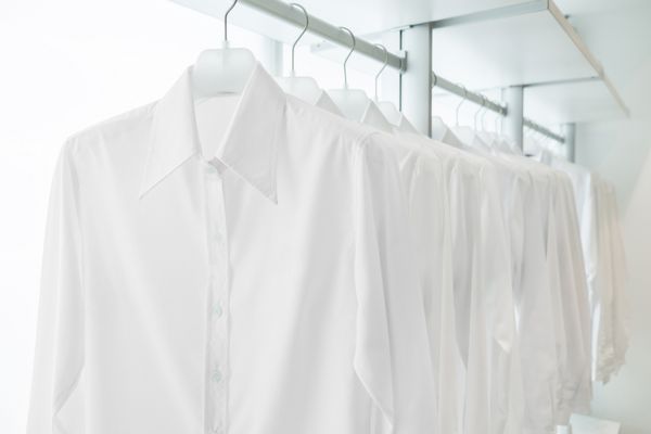 پیراهن‌های سفید آویزان روی قفسه‌های پارچه‌ای توکار سفید با کشو و سایر لوازم جانبی