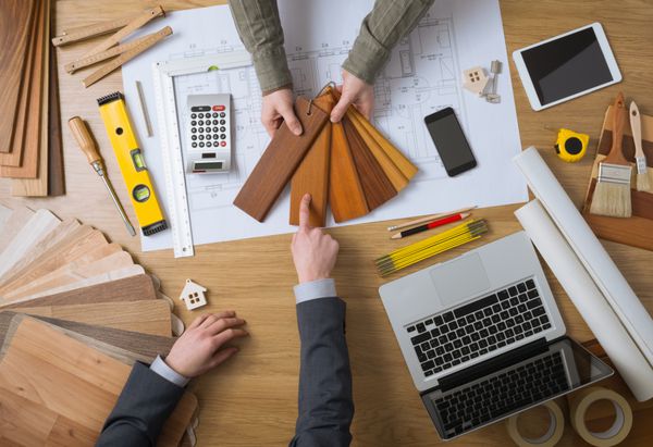 طراح داخلی در حال نمایش نمونه‌های چوبی به مشتری لپ‌تاپ ابزار و پروژه‌های خانه‌اش در نمای بالای رومیزی