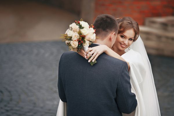 زوج تازه ازدواج کرده خوشبخت با دسته گلی که در فضای باز در آغوش گرفته اند