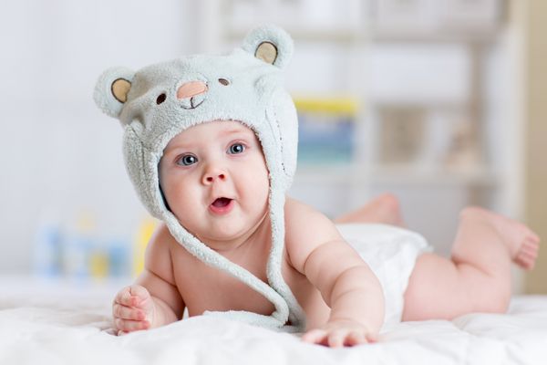 دختر بچه 5 ماهه با کلاه خنده دار که روی یک پتو دراز کشیده بود