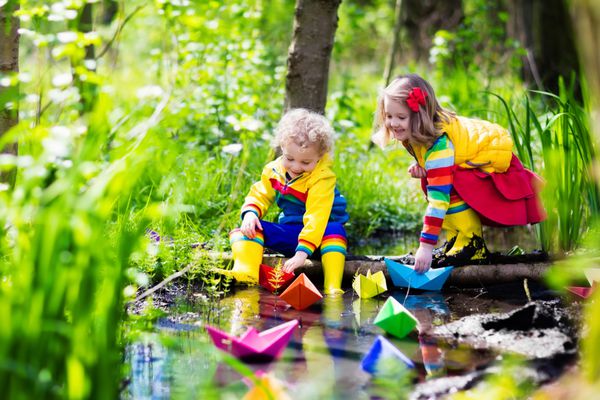 کودکان در یک روز آفتابی بهاری با قایق های کاغذی رنگارنگ در رودخانه ای کوچک بازی می کنند بچه ها در حال کاوش در طبیعت برادر و خواهر در حال تفریح در یک رودخانه جنگلی پسر و دختر با قایق و کشتی اسباب بازی