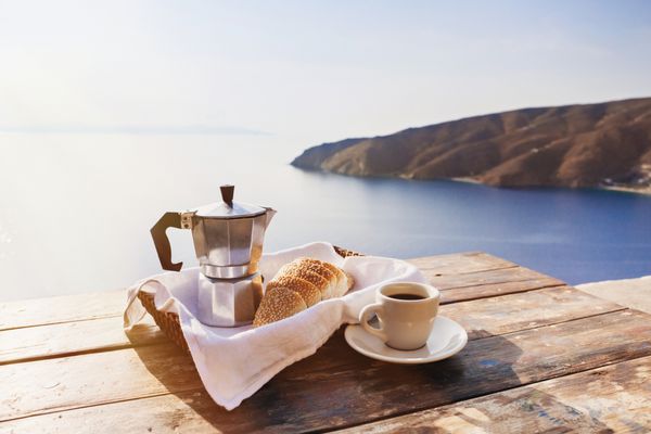 صبحانه مدیترانه ای فنجان قهوه و نان تازه روی میزی با منظره زیبای دریا در پس زمینه