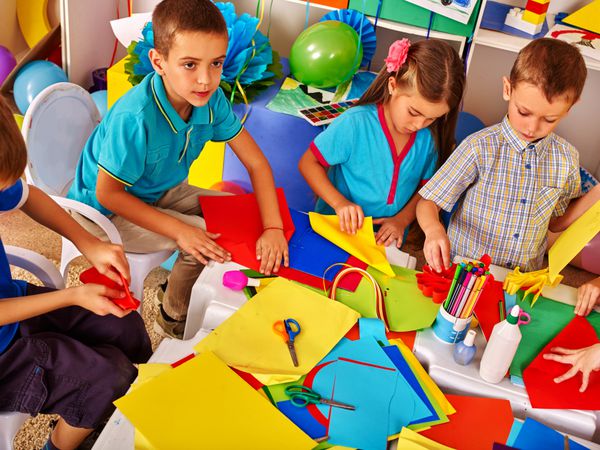 کار کودکان با کاغذ رنگی روی میز در مهدکودک رشد خلاقیت کودکان