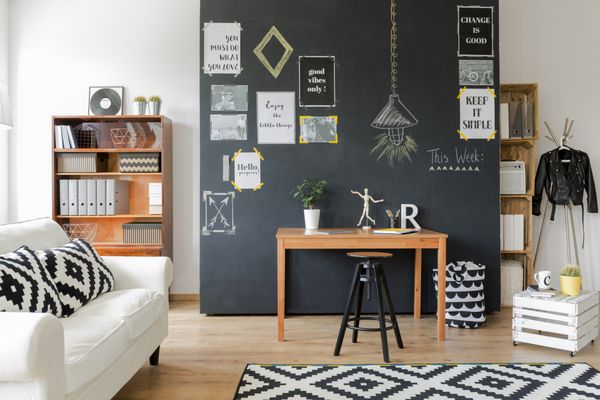 اتاقی با طراحی مدرن با دیوار مشکی با پوسترهای انگیزشی با میز چوبی صندلی مینیمالیستی قفسه‌ها کاناپه سفید با کوسن و فرش با موضوع موزاییک