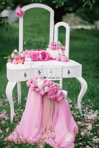 میز آرایش و صندلی سفید با تزئینات گلدار در فضای باز ایستاده است