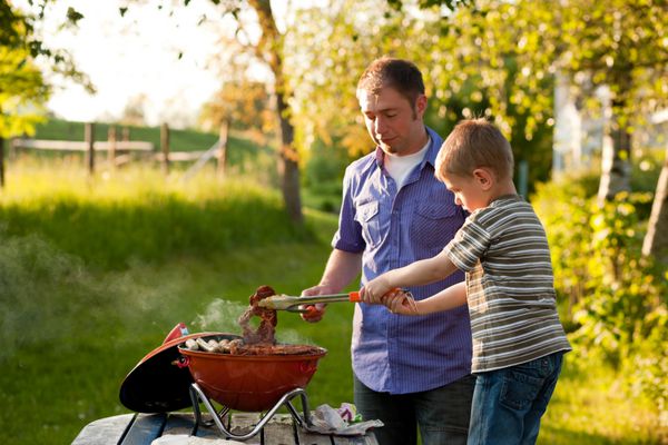 خانواده - پدر و پسر - مهمانی کباب کردن کودک در حال چرخاندن گوشت و سوسیس هر دو سرگرمی