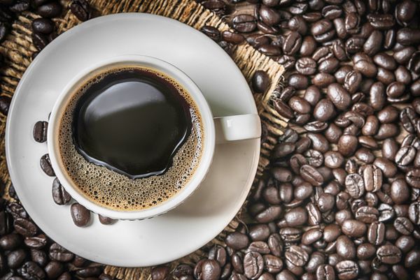 فنجان قهوه و دانه های قهوه روی میز چوبی