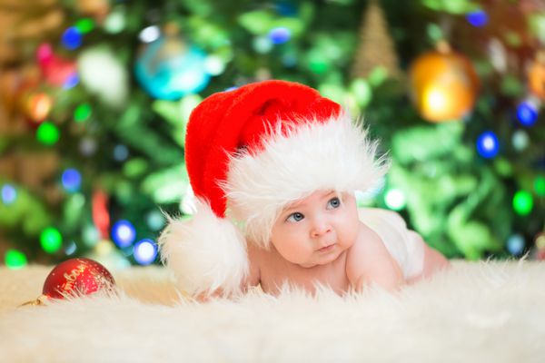 کودک کوچک با کلاه قرمز بابانوئل کریسمس را جشن می گیرد عکس کریسمس نوزاد با کلاه قرمز تعطیلات سال نو و درخت کریسمس