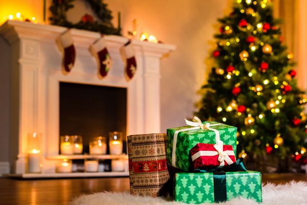 چند هدیه زیبای کریسمس در اتاق نشیمن پر از فضای جادویی تعطیلات زمستانی تزئین شده با روبان در کنار آتش دنج گرم پس زمینه کریسمس و تعطیلات زمستانی