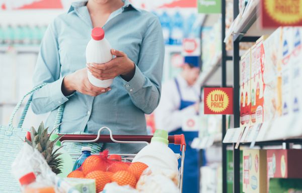 زنی در حال خرید مواد غذایی در سوپرمارکت و خواندن برچسب های مواد غذایی مفهوم تغذیه و کیفیت