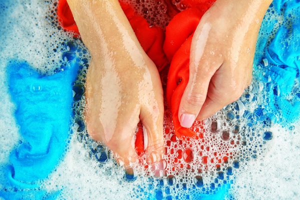 دست های زن در حال شستن لباس های رنگی در لگن