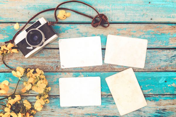 دوربین رترو و آلبوم عکس کاغذ فوری خالی قدیمی روی میز چوبی با طرح حاشیه گل - مفهوم خاطره و نوستالژی در بهار سبک وینتیج