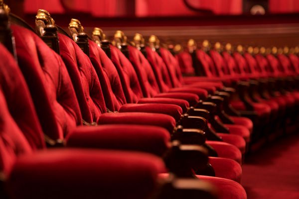 صندلی‌های سینمای اپرا از مخمل‌های قرمز عمیق و مخملی با چوب تزئینی سنتی کلاسیک سلطنتی در سالن نمایش با فرش فانتزی با قالب‌های طلایی تزئینی