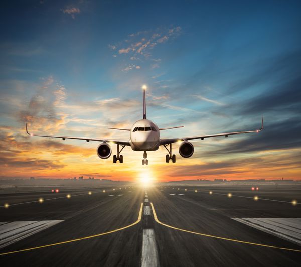 فرود هواپیمای مسافربری به باند فرودگاه در نور زیبای غروب خورشید شبح شهر مدرن در پس زمینه