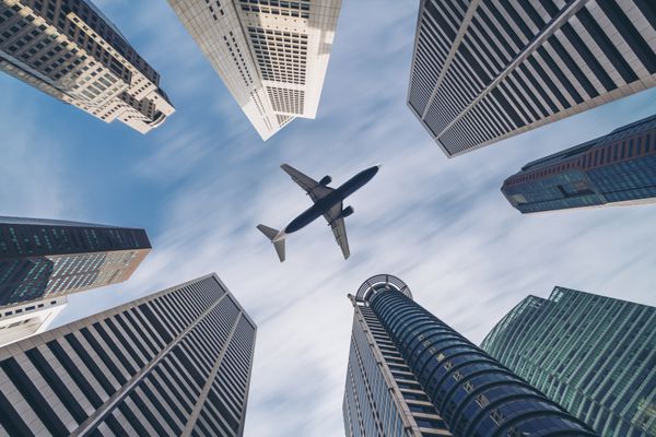 هواپیمای جت در حال حرکت در آسمان بر فراز ساختمان های شهری در مرکز شهر مقصد مسافرتی شهر سنگاپور نمایش مفهوم حمل و نقل گردشگری ساخت هواپیما و تجارت هواپیمایی