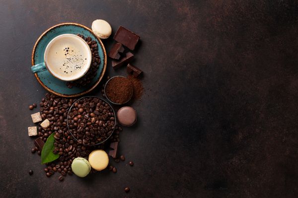 فنجان قهوه دانه ها و پودر آسیاب شده شکلات و ماکارون در زمینه سنگی نمای بالا با فضای کپی برای متن شما